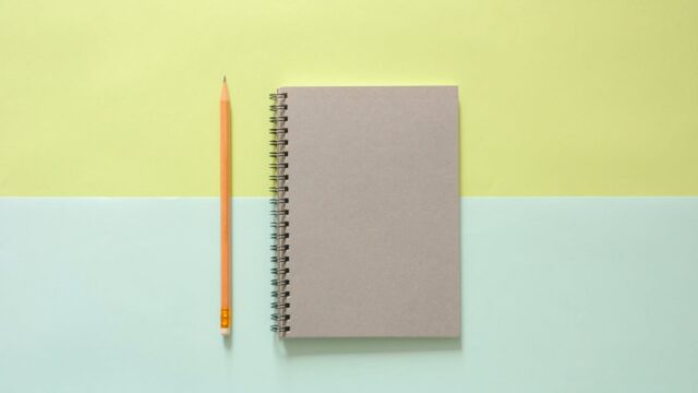 white spiral notebook beside orange pencil