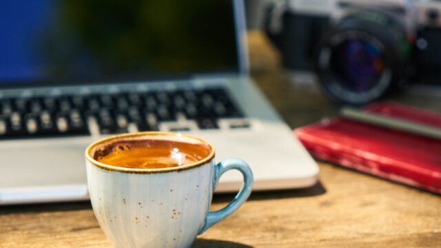 a cup of coffee and a camera on a wooden table in the workplace